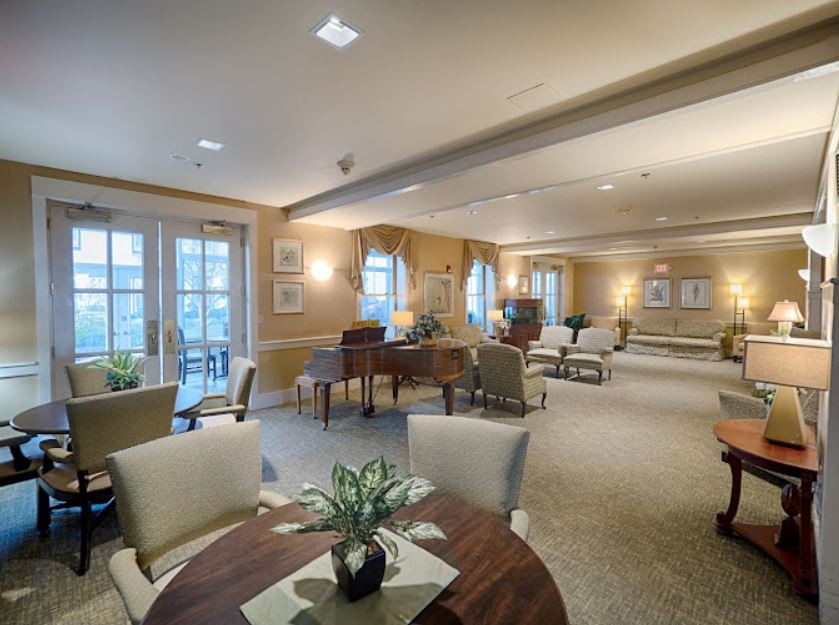 A spacious and cozy lounge area featuring a piano, various seating arrangements, and large windows.