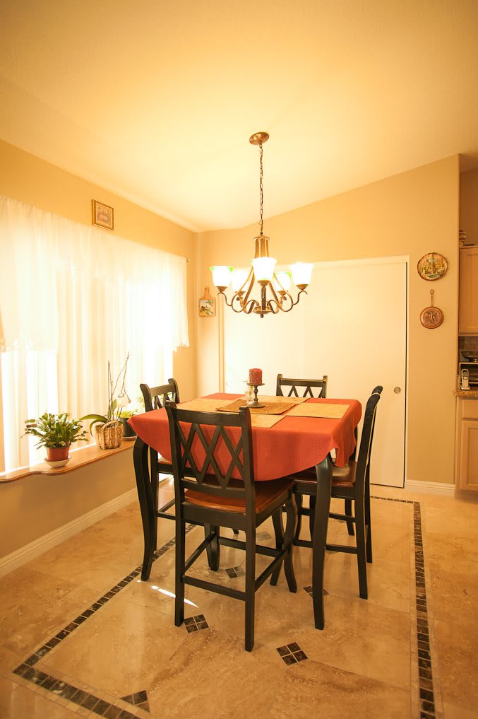 A cozy dining room with a table set for four, illuminated by a chandelier and natural light from a large window.