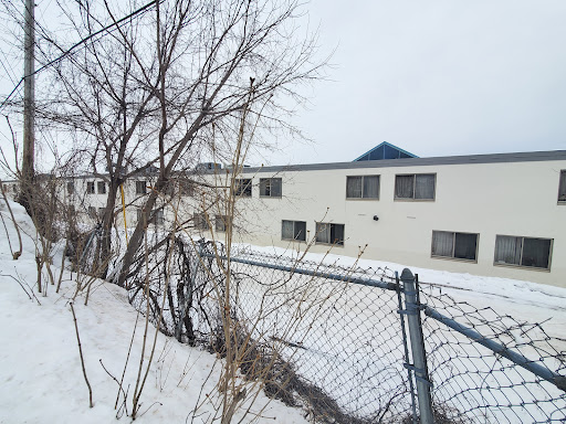 A view of a snow-covered building surrounded by a fence and bare trees on a winter day.