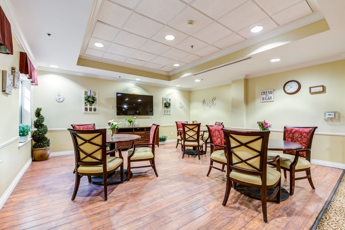 A well-lit dining area featuring several tables and chairs, with a television mounted on the wall.
