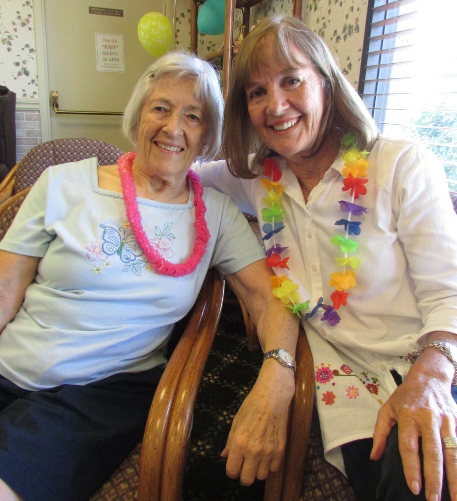 Two women smiling and enjoying a festive celebration with leis.