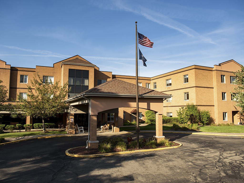 A hotel entrance with a driveway, featuring flags waving on poles.