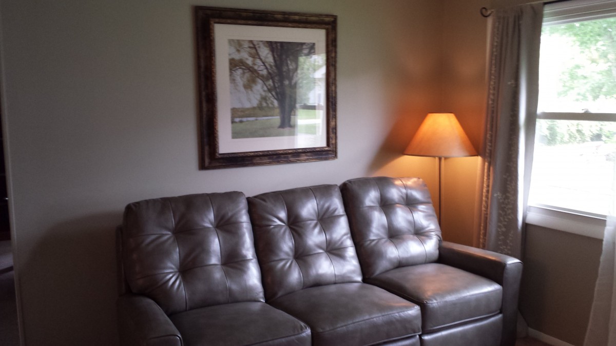 A cozy living room with a leather sofa, a floor lamp, and framed wall art.