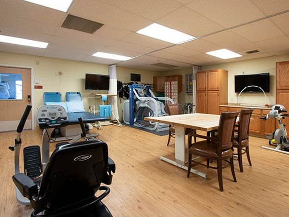A fitness center with various exercise equipment, including a treadmill and chairs around a table.