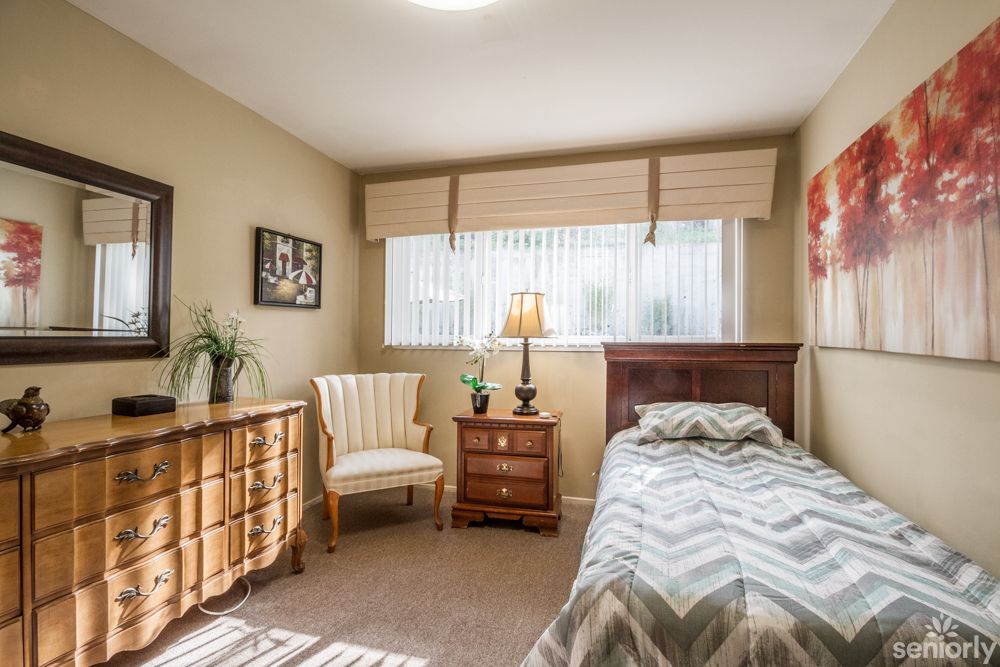 A cozy bedroom with a single bed, dresser, chair, and lamp near a window.