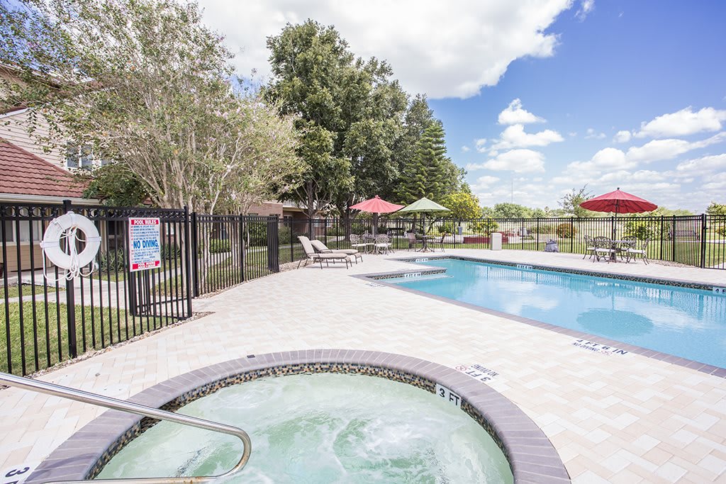 A sunny day view of a swimming pool and hot tub area surrounded by trees and patio furniture.