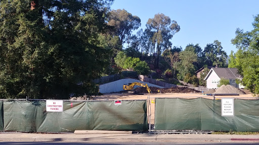 Ongoing demolition work in a residential area, with construction equipment visible behind a green fence.