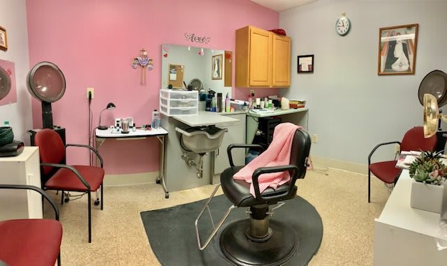 A cozy hair salon with a pink accent wall, a comfortable barber chair, and a well-organized workspace.