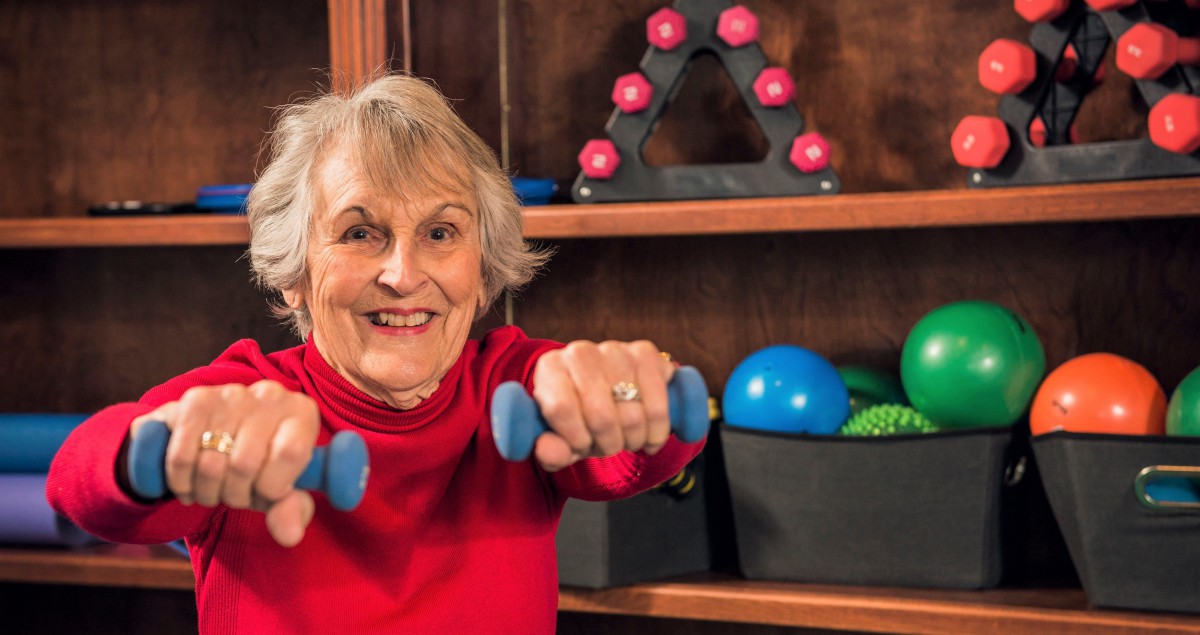 A senior woman smiling while lifting dumbbells as part of her exercise routine.