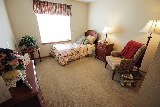 A cozy bedroom with a bed, nightstand, lamp, and armchair.