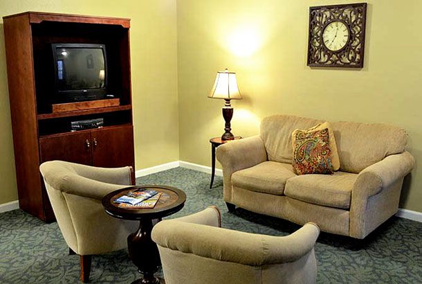 A cozy living room with a sofa, two armchairs, a TV stand, and a coffee table, warmly lit by a standing lamp.