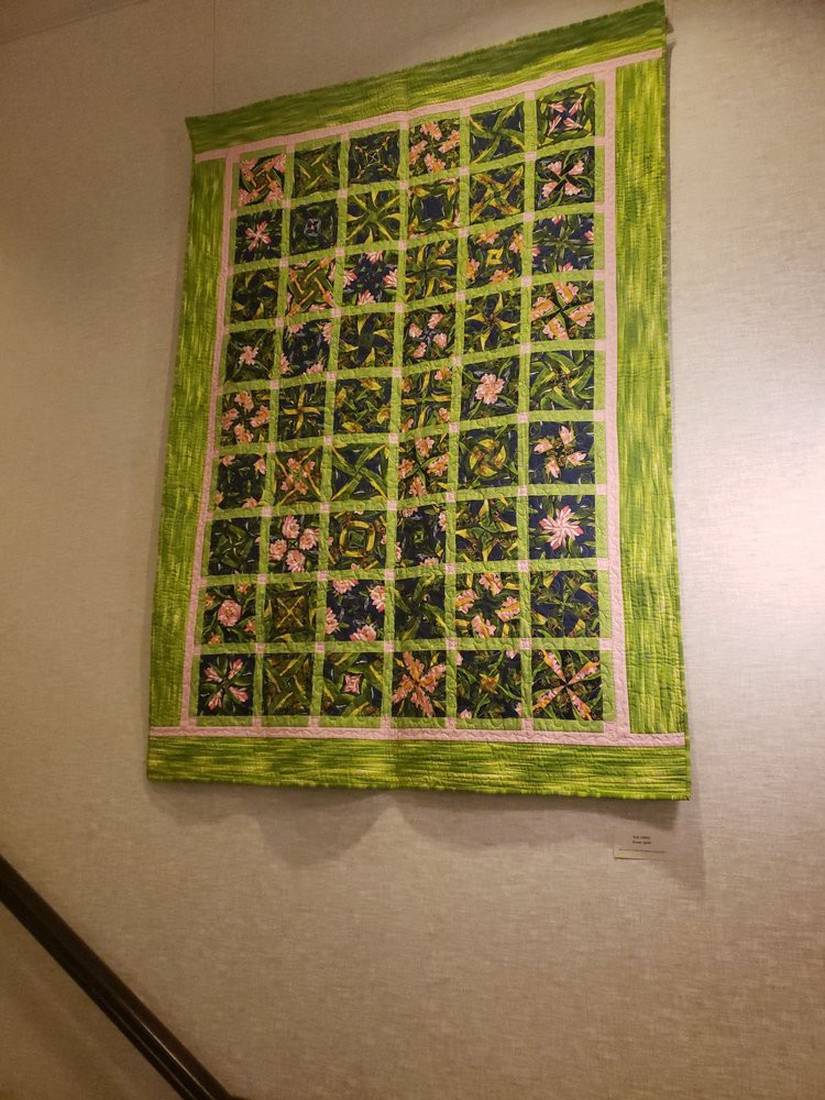 A colorful quilt with a green border hangs on the wall.