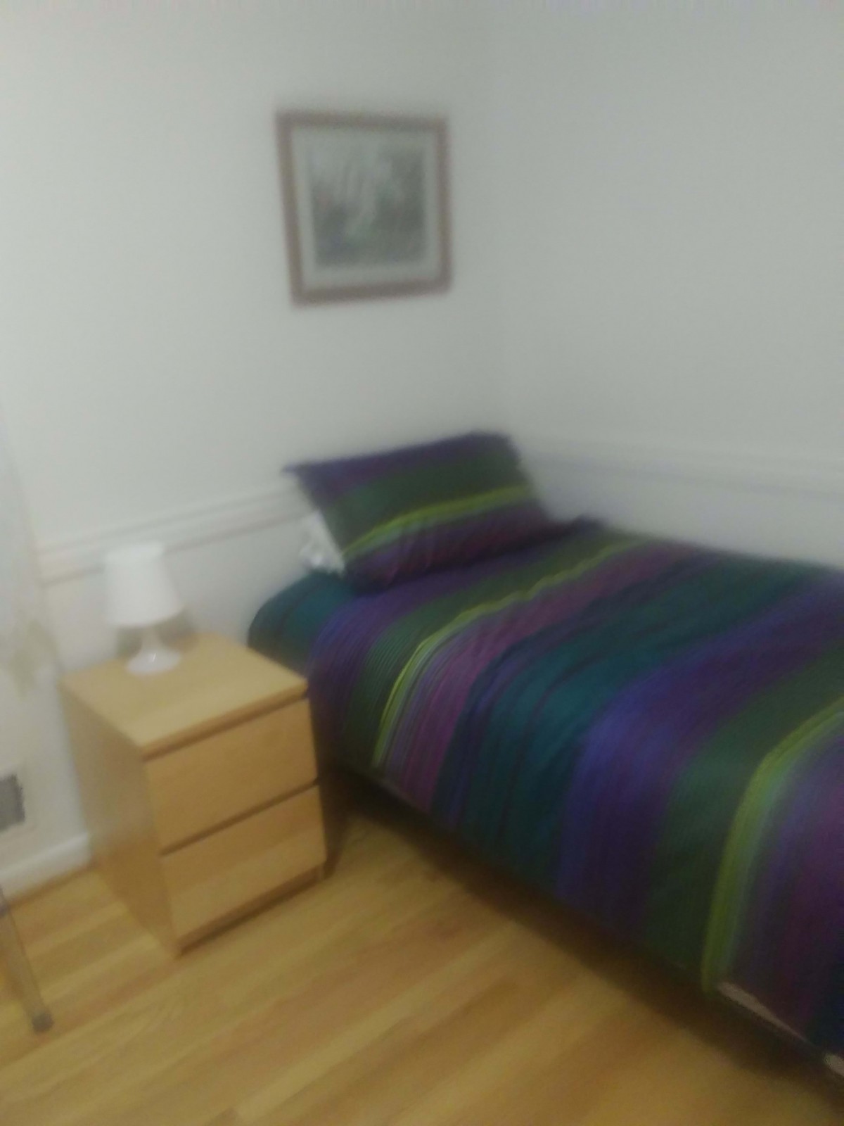 A cozy bedroom with a single bed adorned with striped bedding, next to a wooden nightstand and lamp.