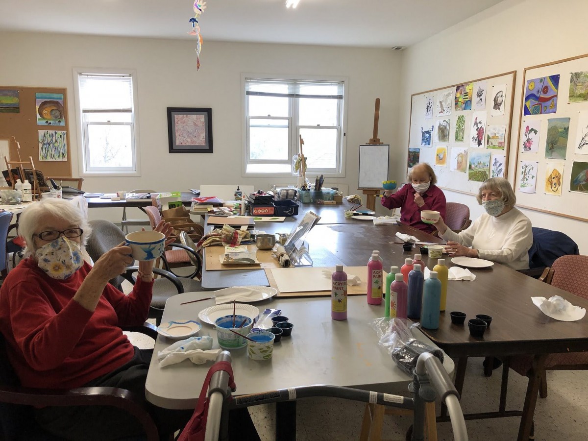 A group of people engaging in an art class, painting and crafting together around a table.