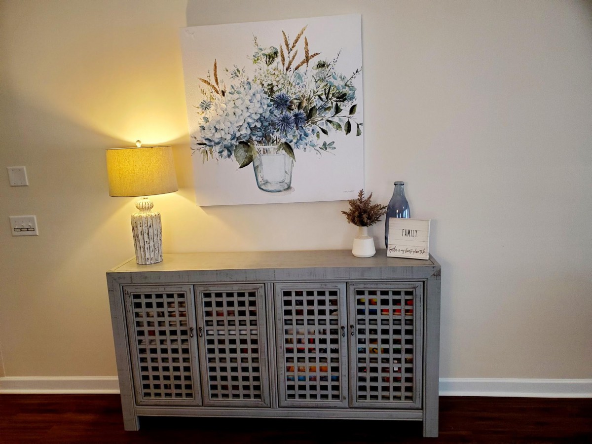A stylish hallway setup featuring a gray cabinet, decorative lamp, and floral artwork.