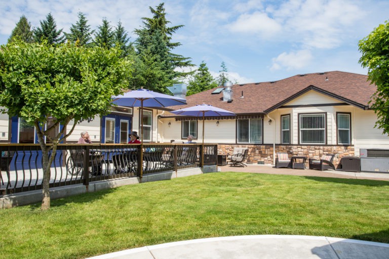 A cozy backyard patio area with outdoor seating and umbrellas, surrounded by a well-maintained lawn and trees.