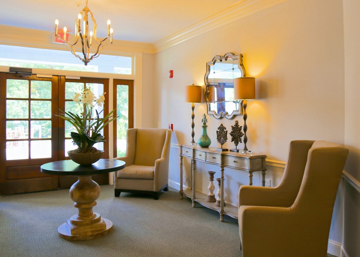 A luxurious living room with elegant furnishings, including upholstered chairs, a decorative mirror, a table with a potted plant, and stylish lamps.
