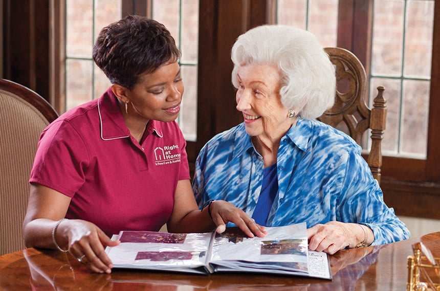 A caregiver and an elderly woman looking at a photo album together.