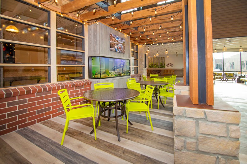 A cozy outdoor cafe area with bright yellow chairs and a wooden ceiling adorned with string lights.