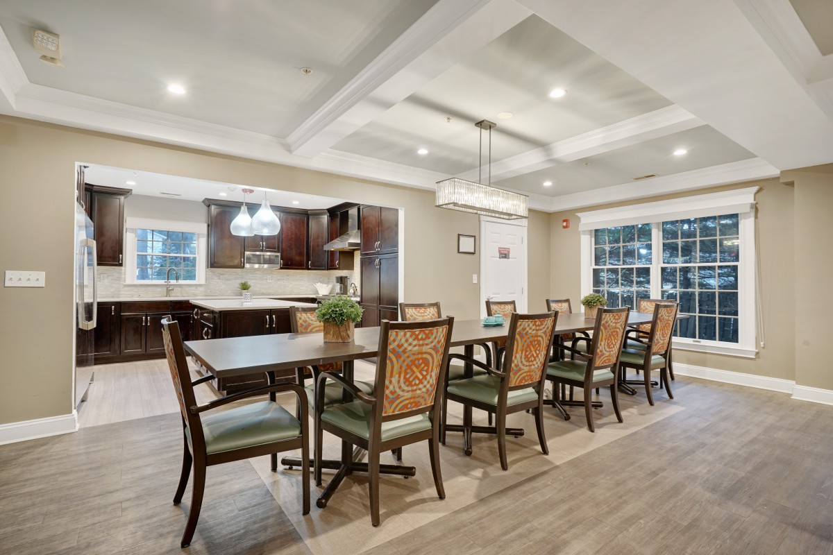 A spacious dining area with modern decor, featuring a large table and several chairs, adjacent to a well-equipped kitchen.
