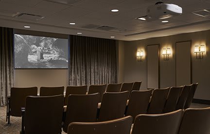 An empty theater room with rows of chairs facing a projection screen.