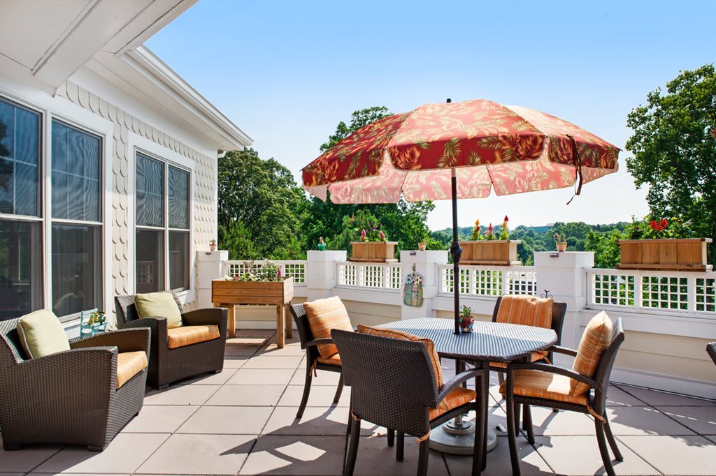A sunny patio featuring comfortable outdoor furniture and a decorative umbrella, with a scenic view in the background.