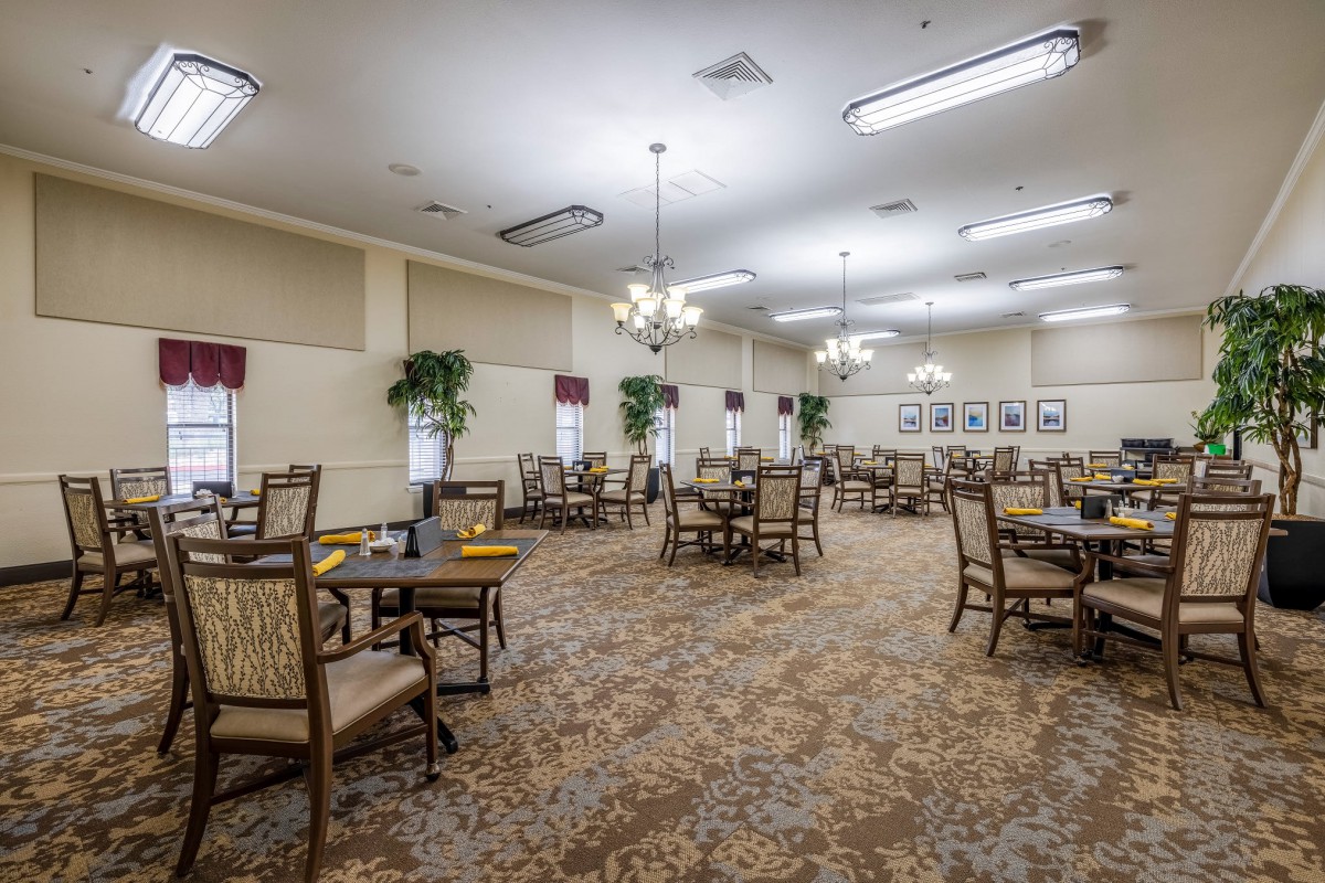 An empty dining room with tables and chairs, decorated with chandeliers and plants.