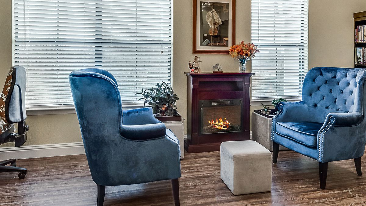 A cozy living room with blue chairs, a fireplace, and large windows.