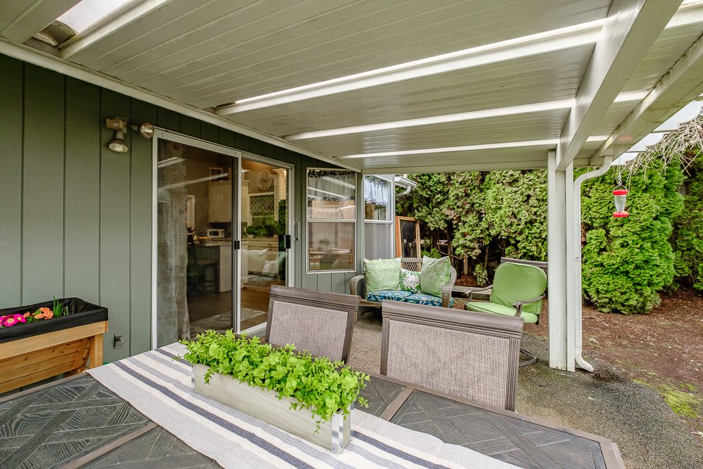 A cozy patio with comfortable outdoor seating under a covered area, surrounded by lush greenery.