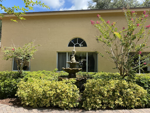 A serene outdoor scene featuring a fountain surrounded by lush greenery in front of a yellow building.