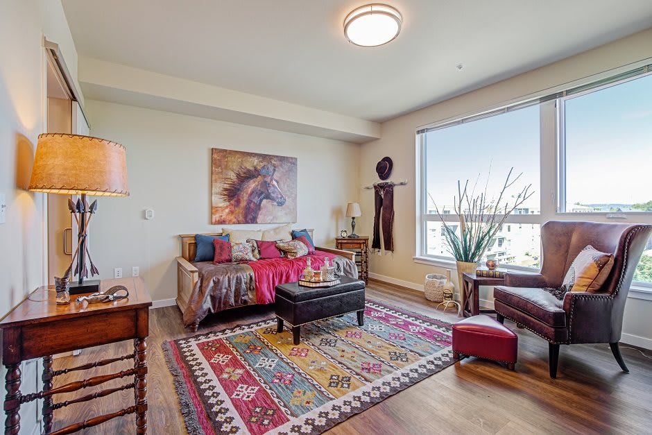 A cozy living room with bohemian decor featuring a colorful rug, vibrant textiles, and large window providing natural light.