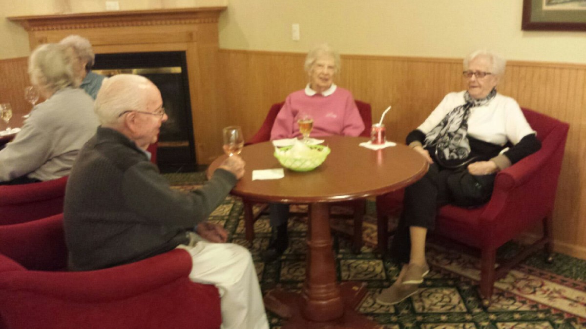 A group of elderly people socializing around a table indoors.
