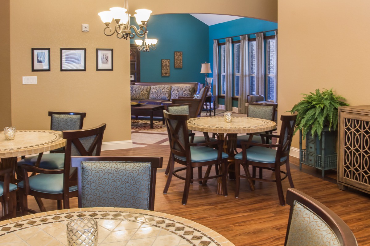 A cozy dining area with round tables and blue-accented chairs, enhanced by warm lighting from a chandelier.