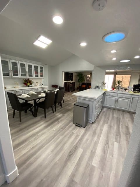 A modern open-layout kitchen and dining area with white cabinets, an island, and skylights.