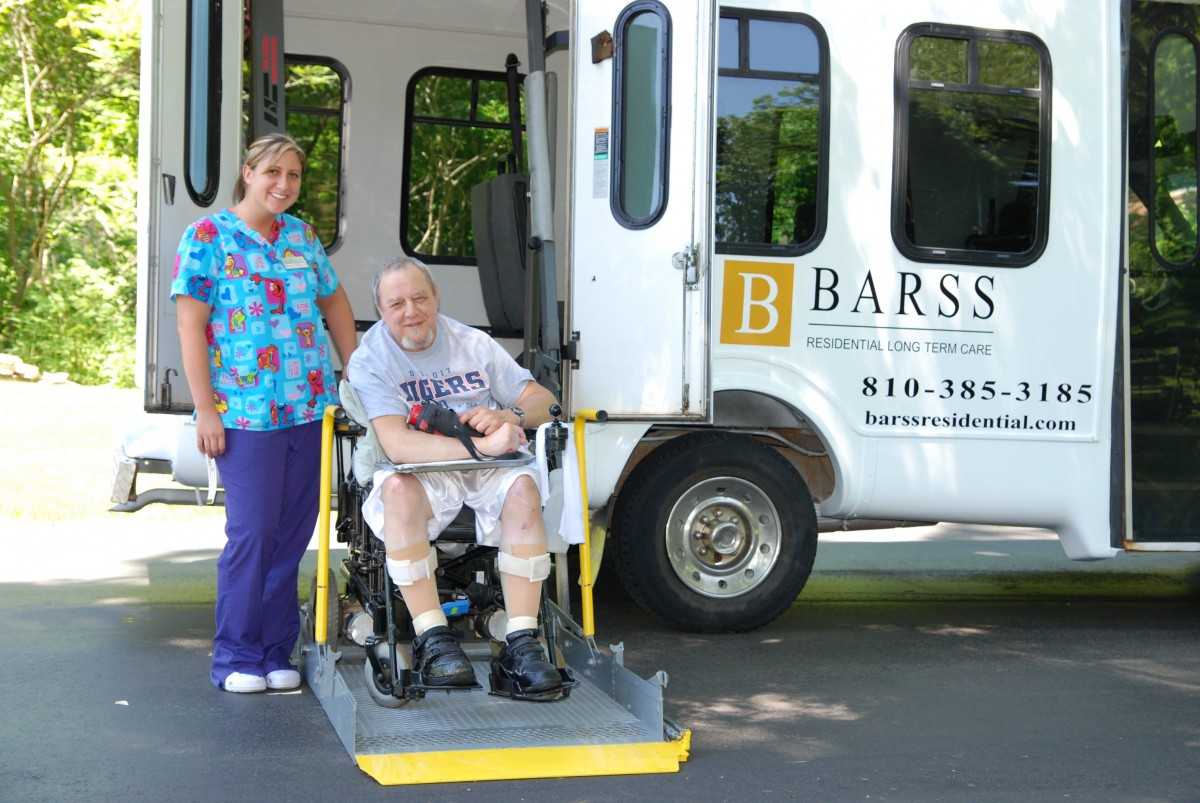 A caregiver assists a person in a wheelchair onto an accessible transport vehicle.