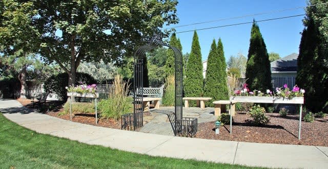 A landscaped garden with benches, a pathway, and an archway under a clear blue sky.