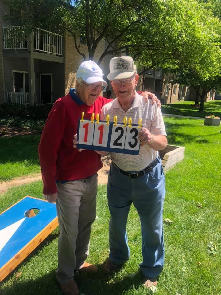 Two elderly individuals standing outdoors holding a scoreboard.