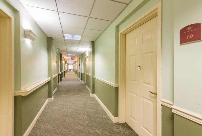 A long, carpeted hallway with doors on either side and overhead ceiling tiles.