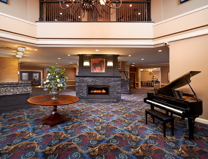 A spacious hotel lobby featuring a grand piano, a stone fireplace, and elegant decor.