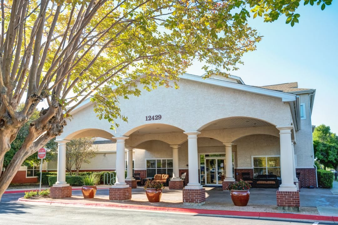 A building entrance with arches and potted plants, surrounded by trees.