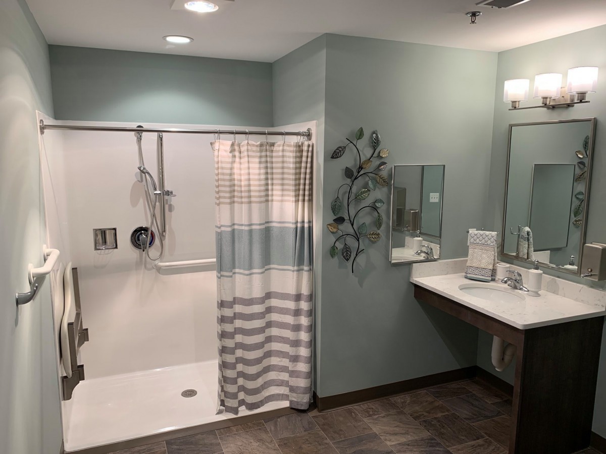 A modern and accessible bathroom featuring a walk-in shower with a striped curtain, a mirror above the sink, and neatly arranged towels.