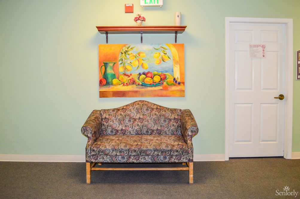 A patterned sofa sits beneath a colorful still-life painting in a well-lit room.
