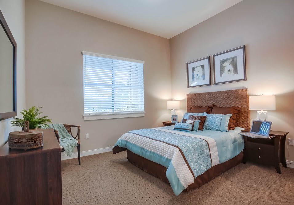 A cozy bedroom with a neatly made bed, nightstand with a lamp, and art pieces on the wall.