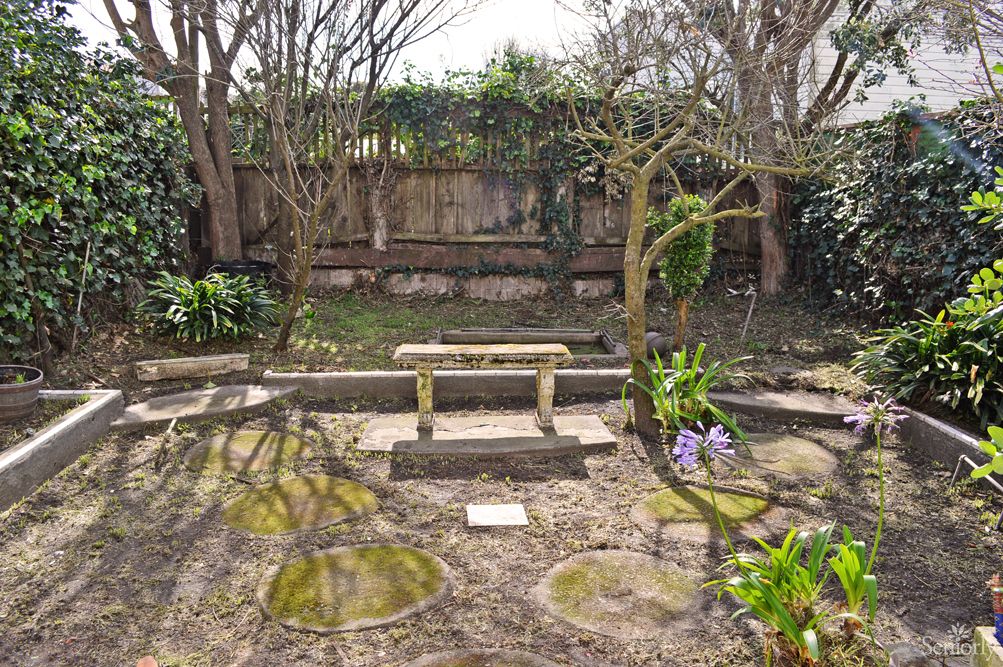 A serene garden featuring a stone bench, surrounded by trees and blooming flowers.