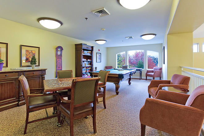 A cozy game room with a pool table, chairs, and a bookshelf.