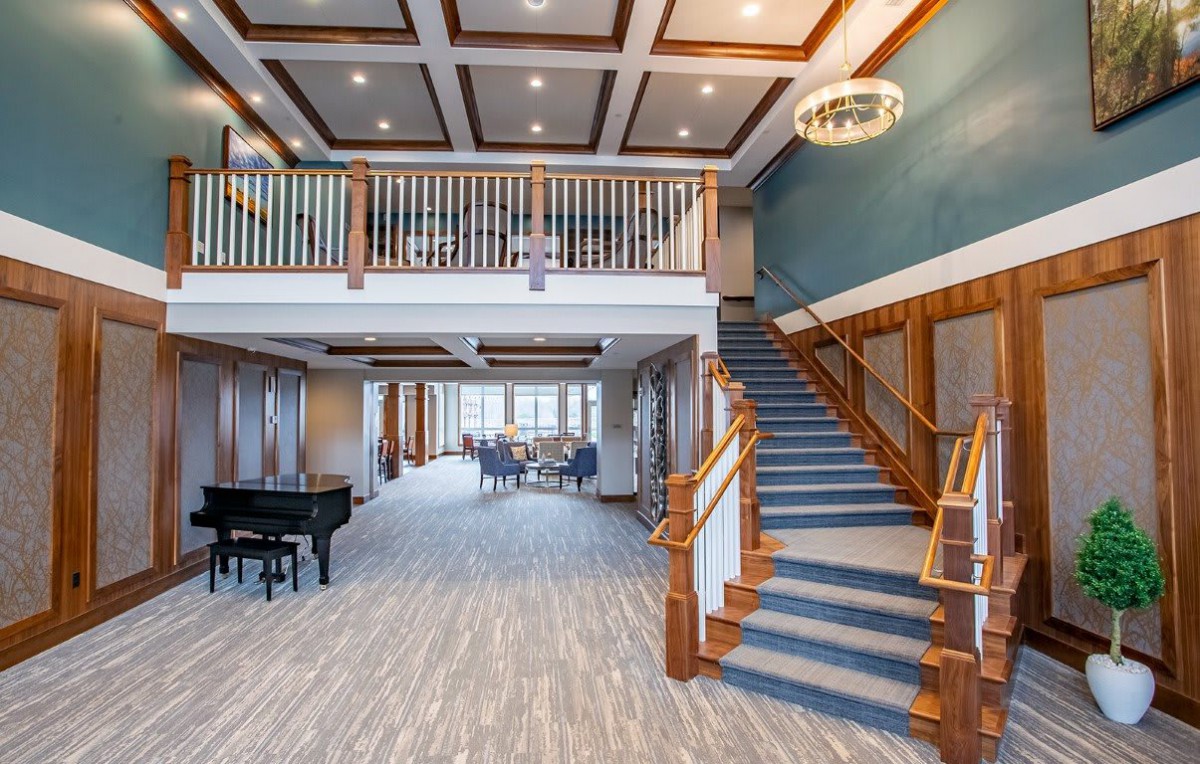 A spacious and elegant lobby featuring a grand staircase and a piano, designed with modern aesthetics and warm wood accents.