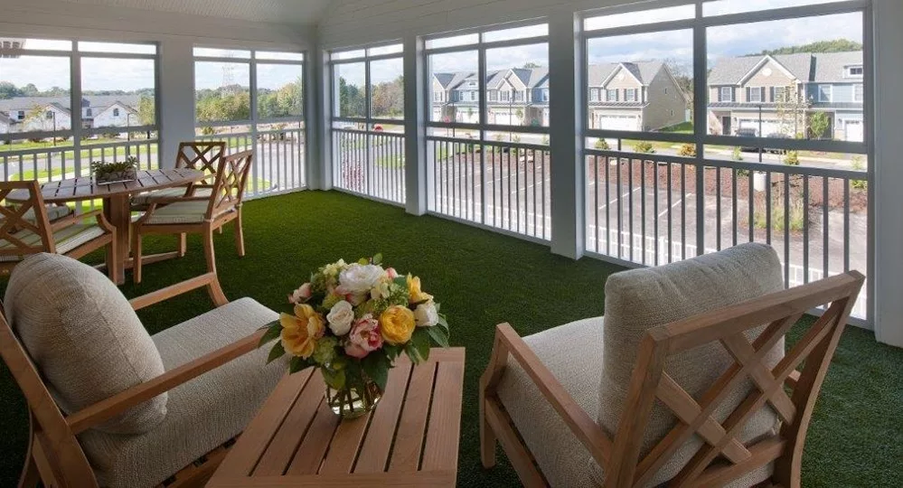 A cozy sunroom with comfortable seating, a floral arrangement on the table, and large windows offering a view of neighboring houses.