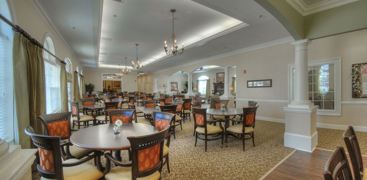 A spacious and elegantly decorated dining area with multiple tables and chairs, featuring chandeliers and a carpeted floor.