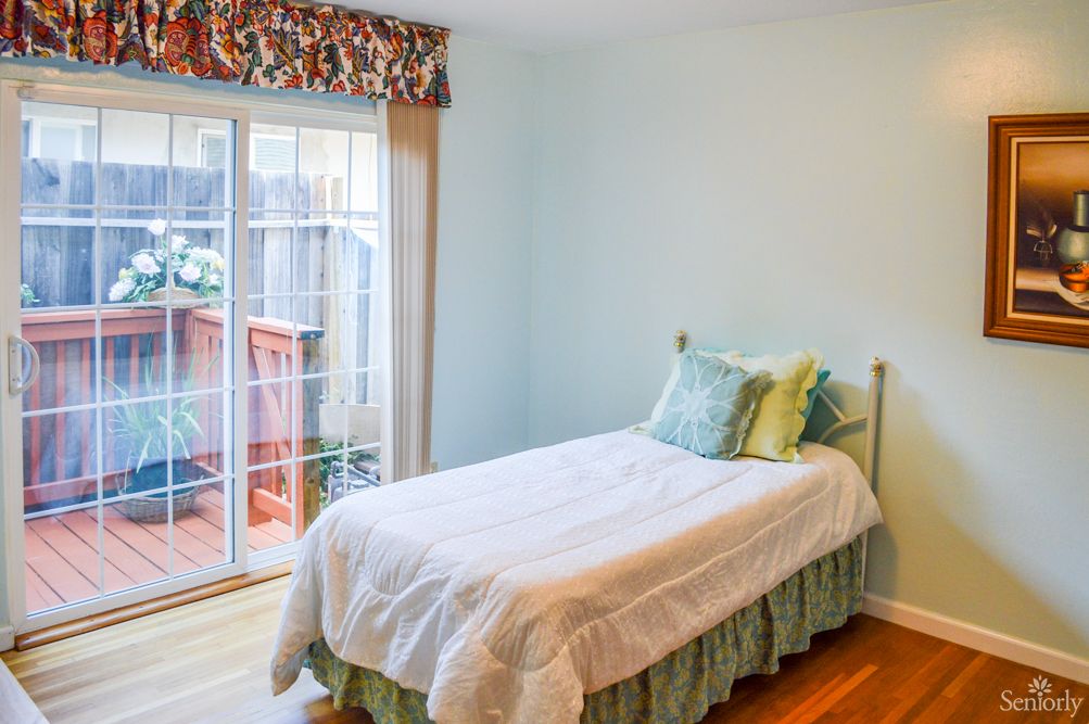 A cozy bedroom with a single bed and a sliding glass door allowing natural light to fill the room.