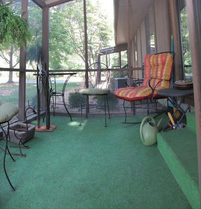 A cozy screened porch with colorful chairs, a green carpet, and plants, perfect for relaxing.